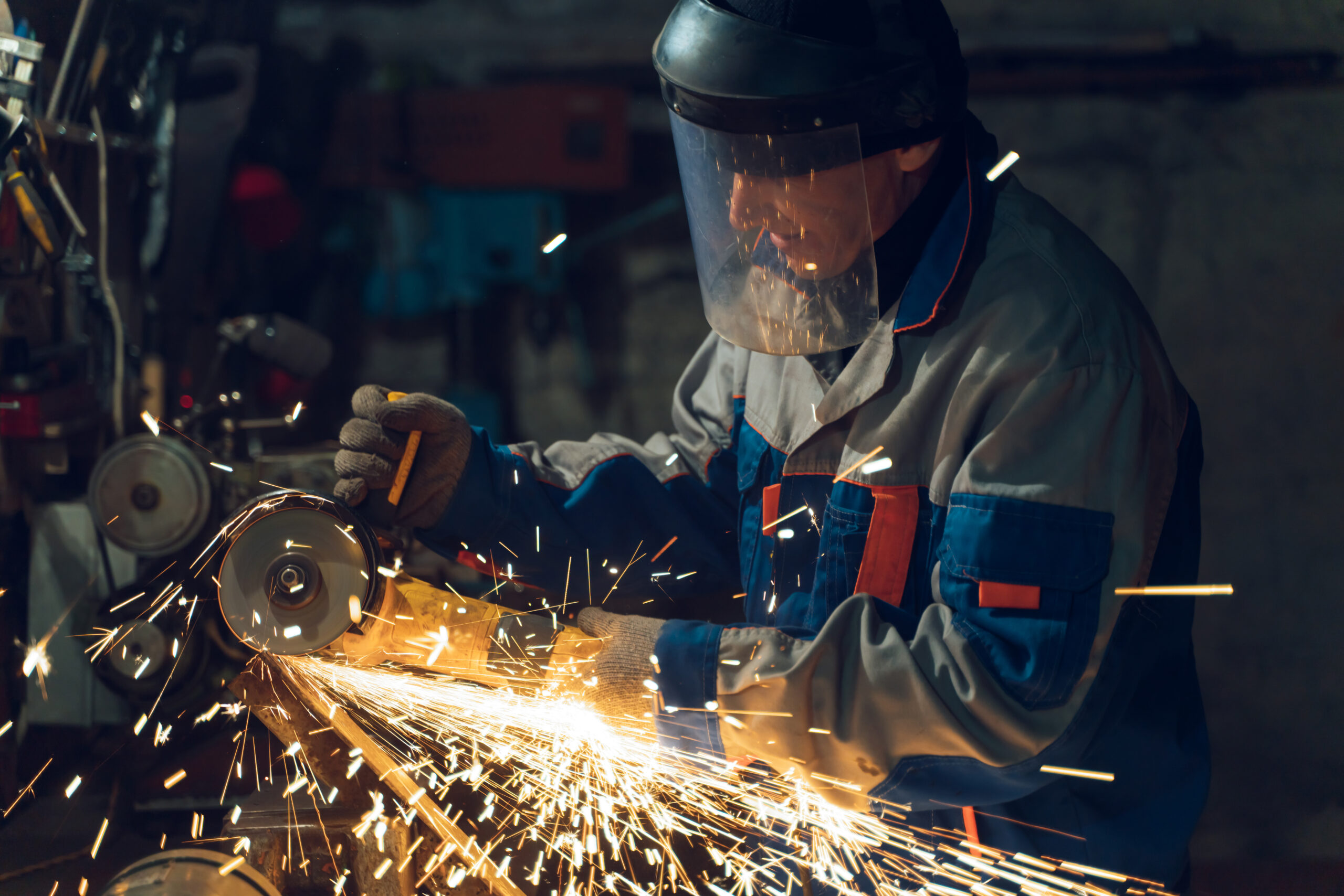 Locksmith in special clothes and goggles works in production. Metal processing with angle grinder. Sparks in metalworking.