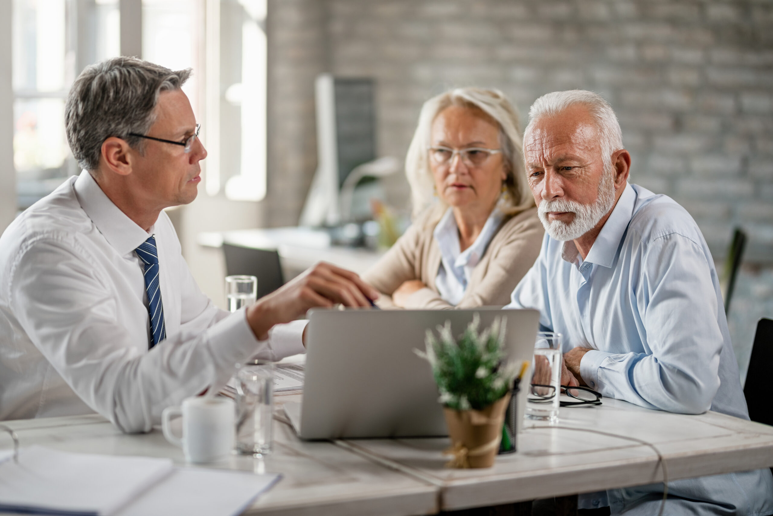 Mature couple and their bank manager using computer while having consultations in the office.